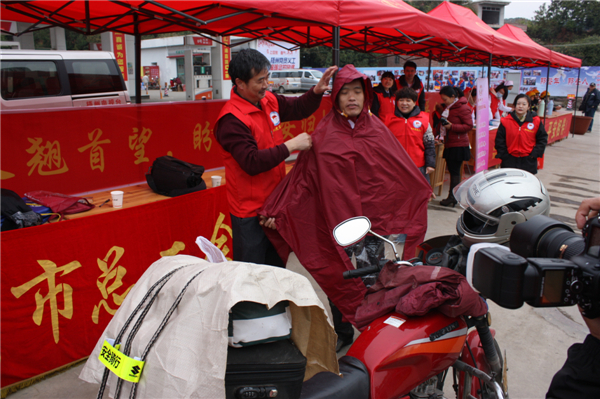 梧州市總工會的黨員義工們在市東出口春運(yùn)服務(wù)站助力“摩托大軍”平安返鄉(xiāng)，幫助他們檢查車輛和行李，穿上雨衣。--黃賀峰攝.j
